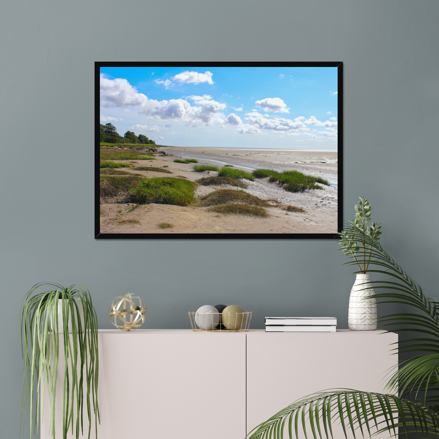 Framed landscape print of a beach scene on a gray wall above a white cabinet with decorative items.