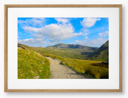 Framed photo of a mountain landscape with a path leading towards distant mountains under a blue sky with clouds