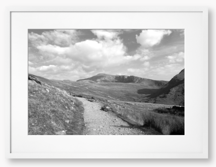 Black and White Framed photo of a mountain landscape with a path leading towards distant mountains with a cloudy sky
