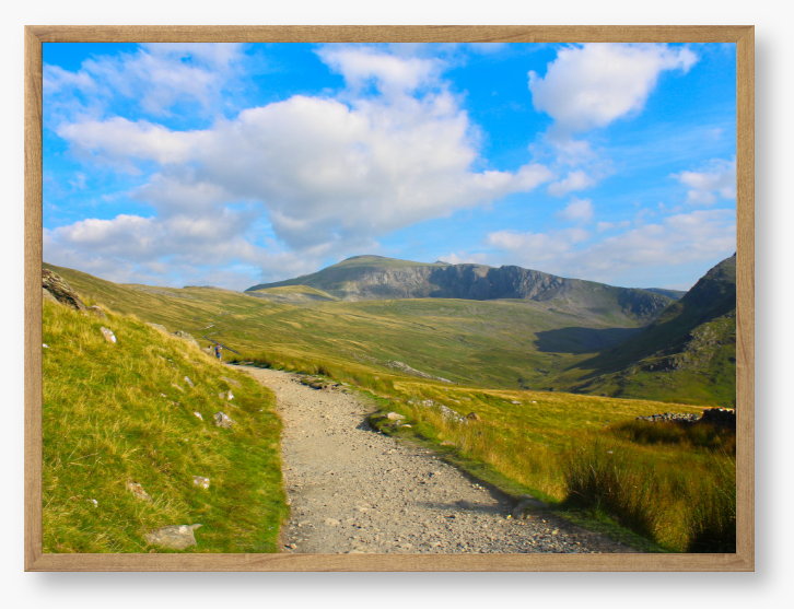 Framed photo of a mountain landscape with a path leading towards distant mountains under a blue sky with clouds