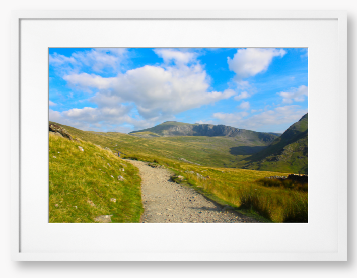 Framed photo of a mountain landscape with a path leading towards distant mountains under a blue sky with clouds