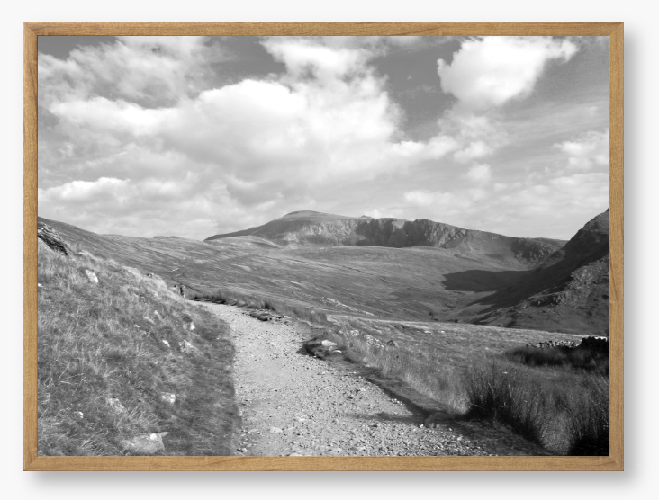 Black and White Framed photo of a mountain landscape with a path leading towards distant mountains with a cloudy sky