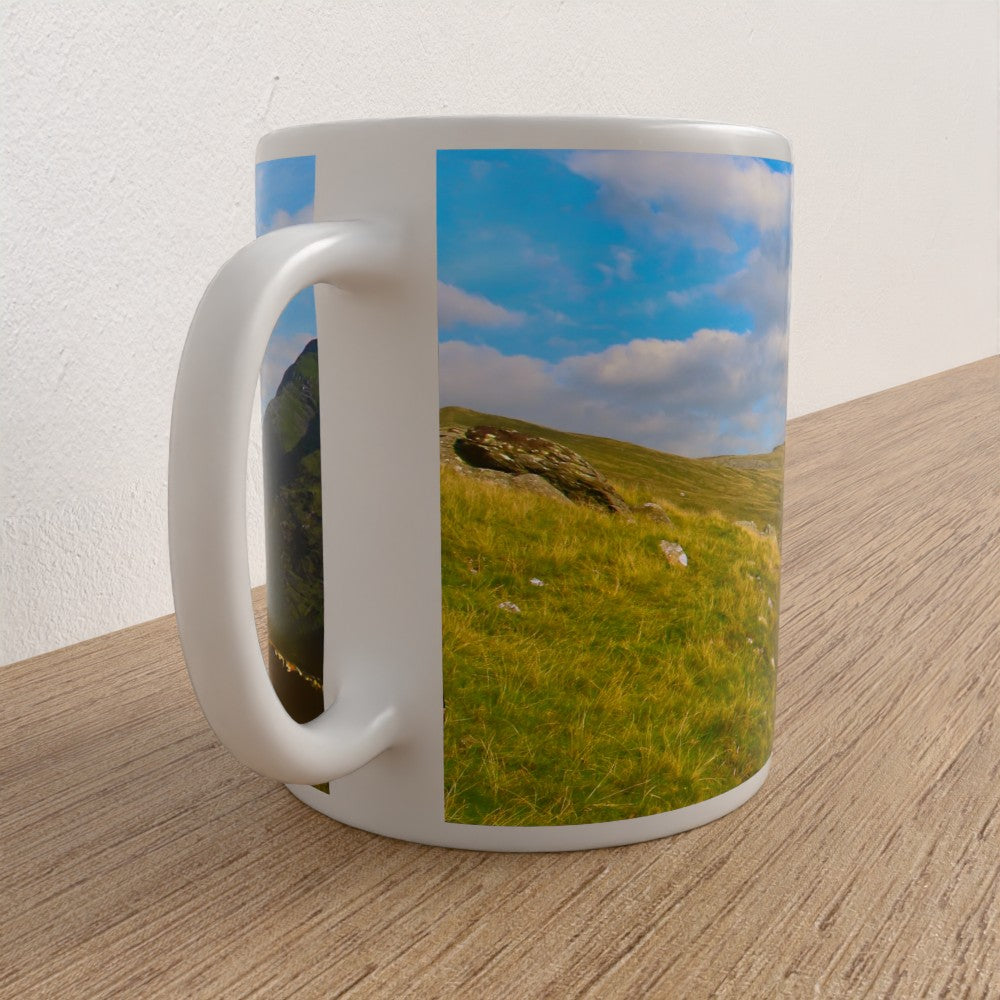 White mug with a scenic design of a grassy hill and blue sky on a wooden surface.