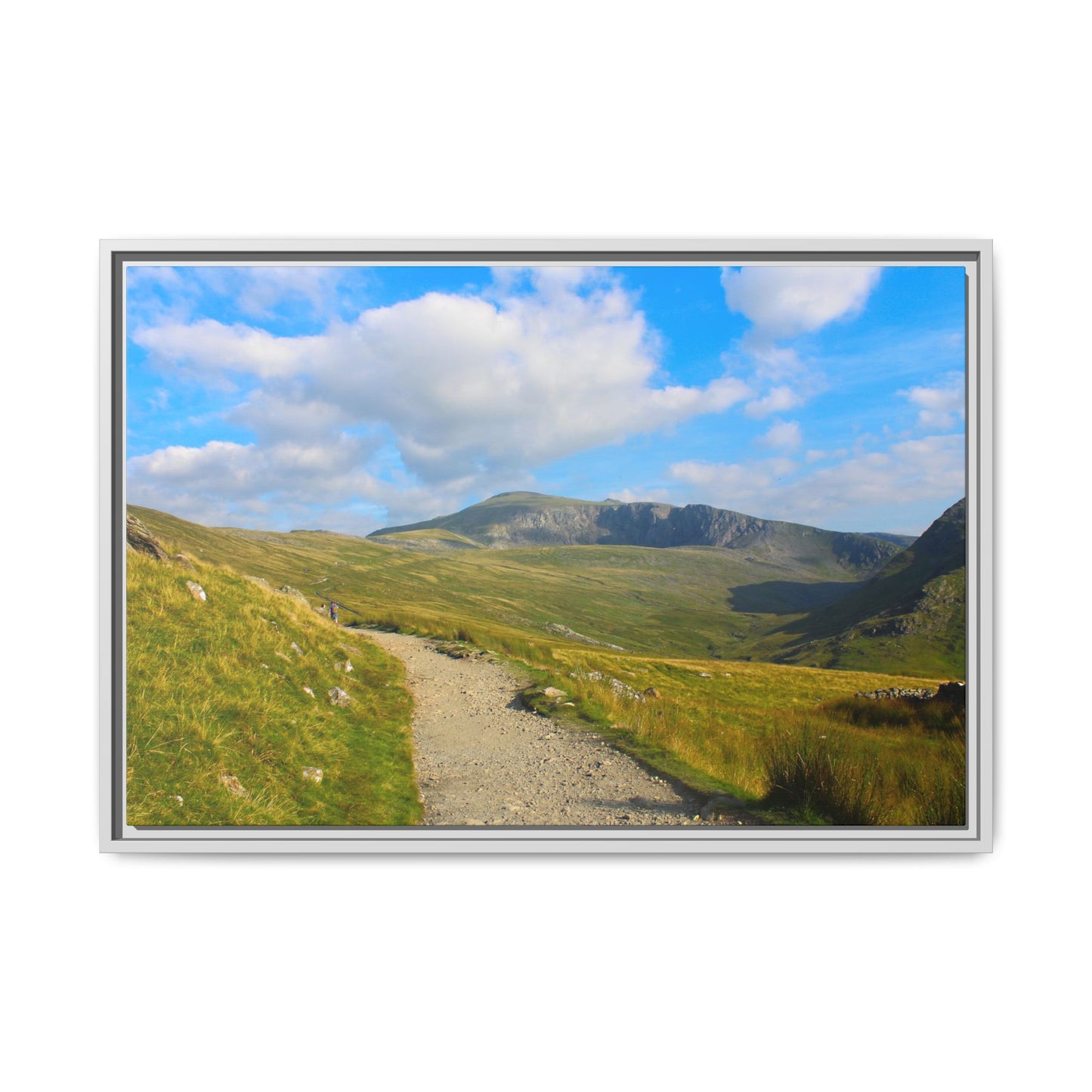 Framed picture of a mountain landscape with a path and blue sky.