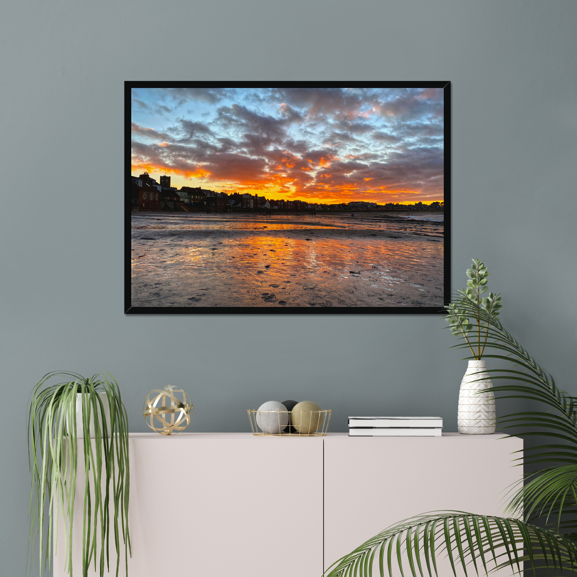 Framed artwork of a sunset over water on a gray wall above a white cabinet with decorative items.