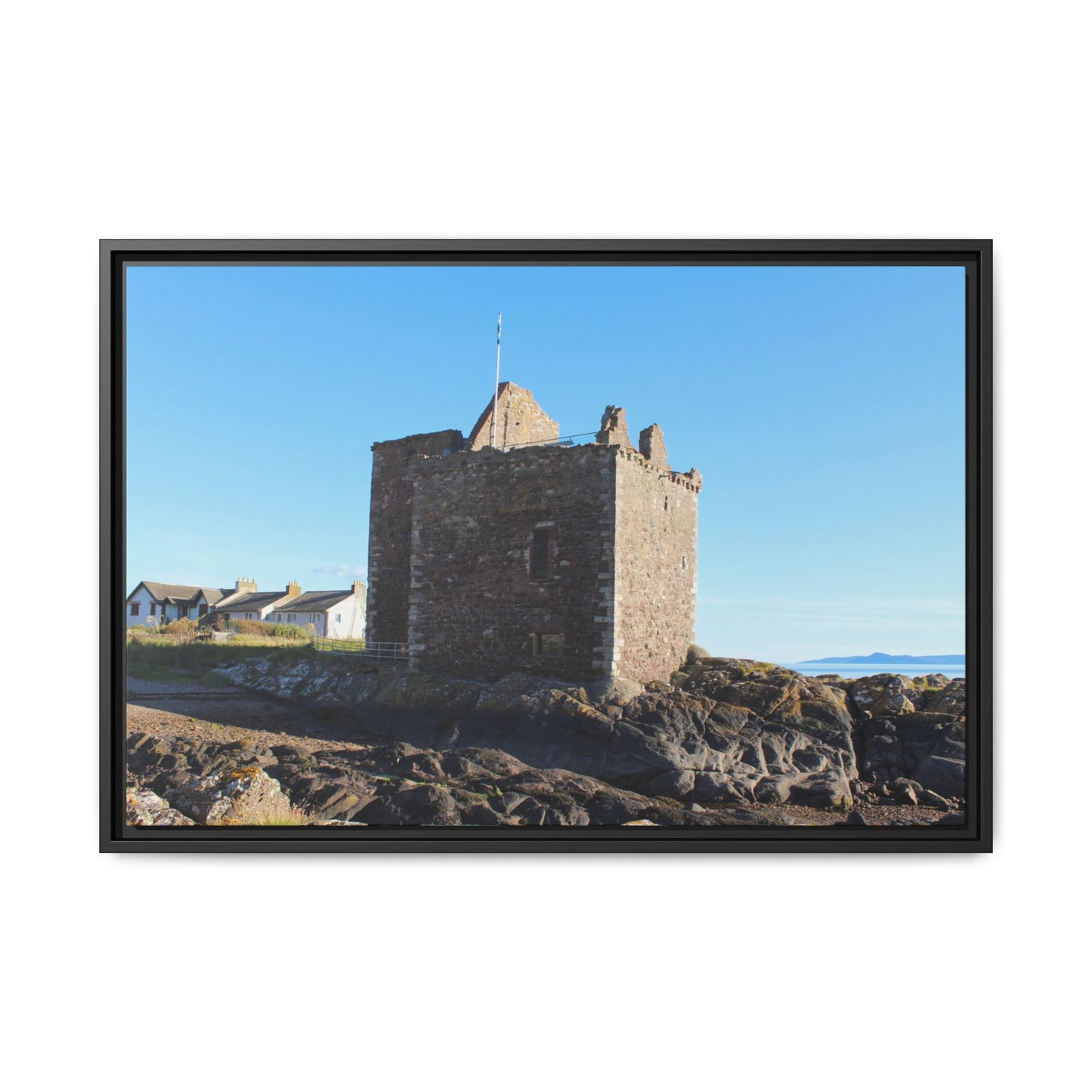 Framed photograph of a stone tower on rocky terrain with a clear blue sky.