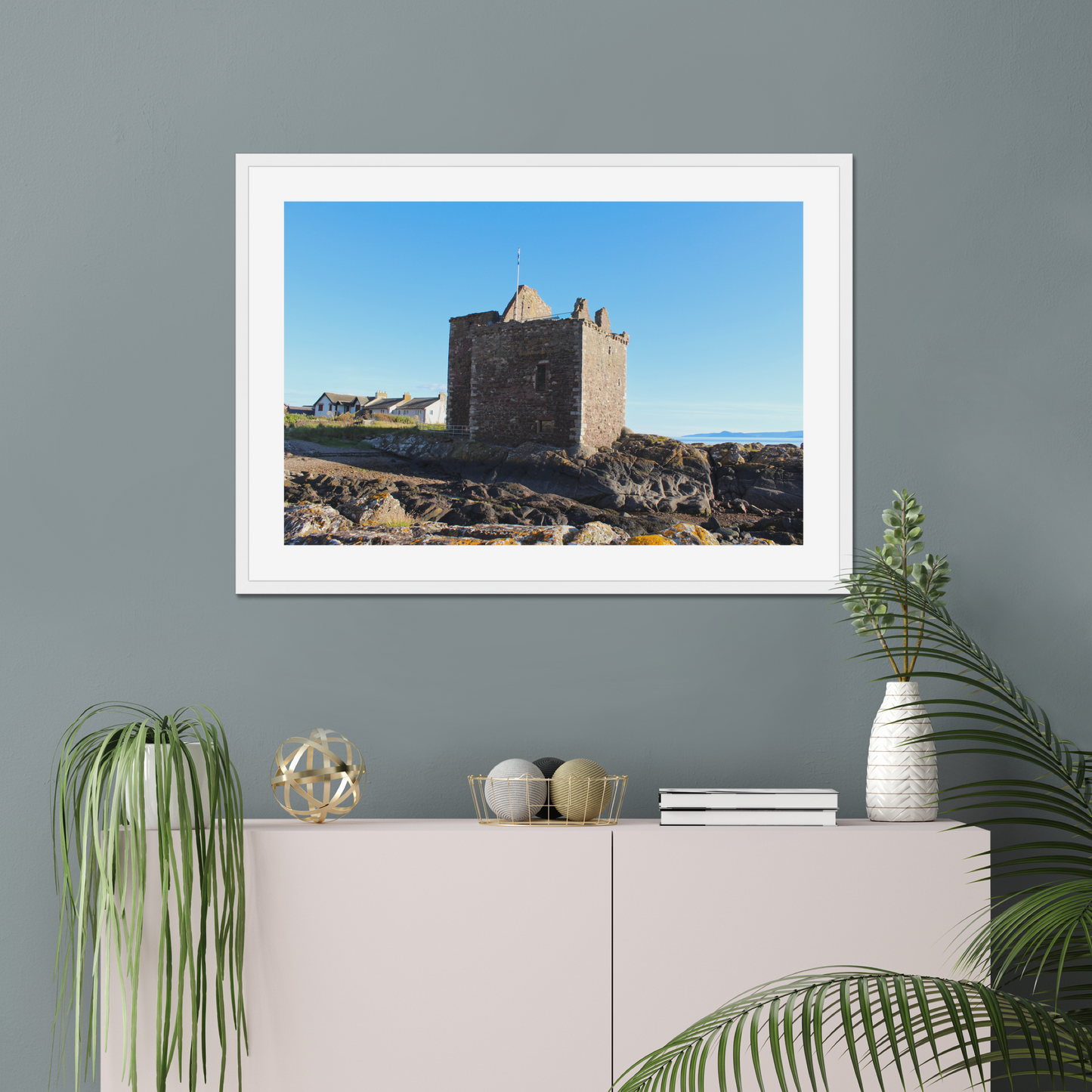 Framed photograph of a castle on a wall above a white cabinet with decorative items.