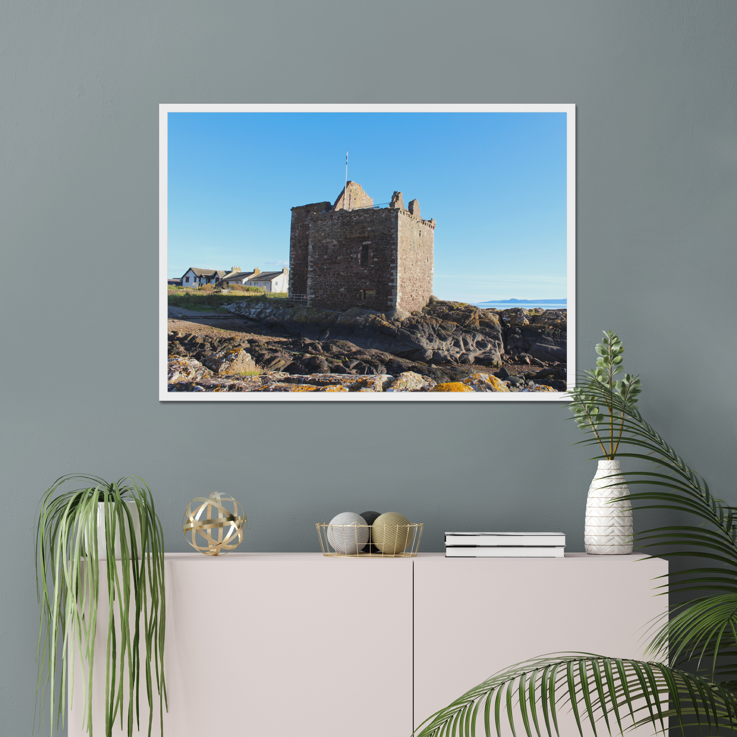 Framed picture of a castle on a wall above a white cabinet with decorative items.