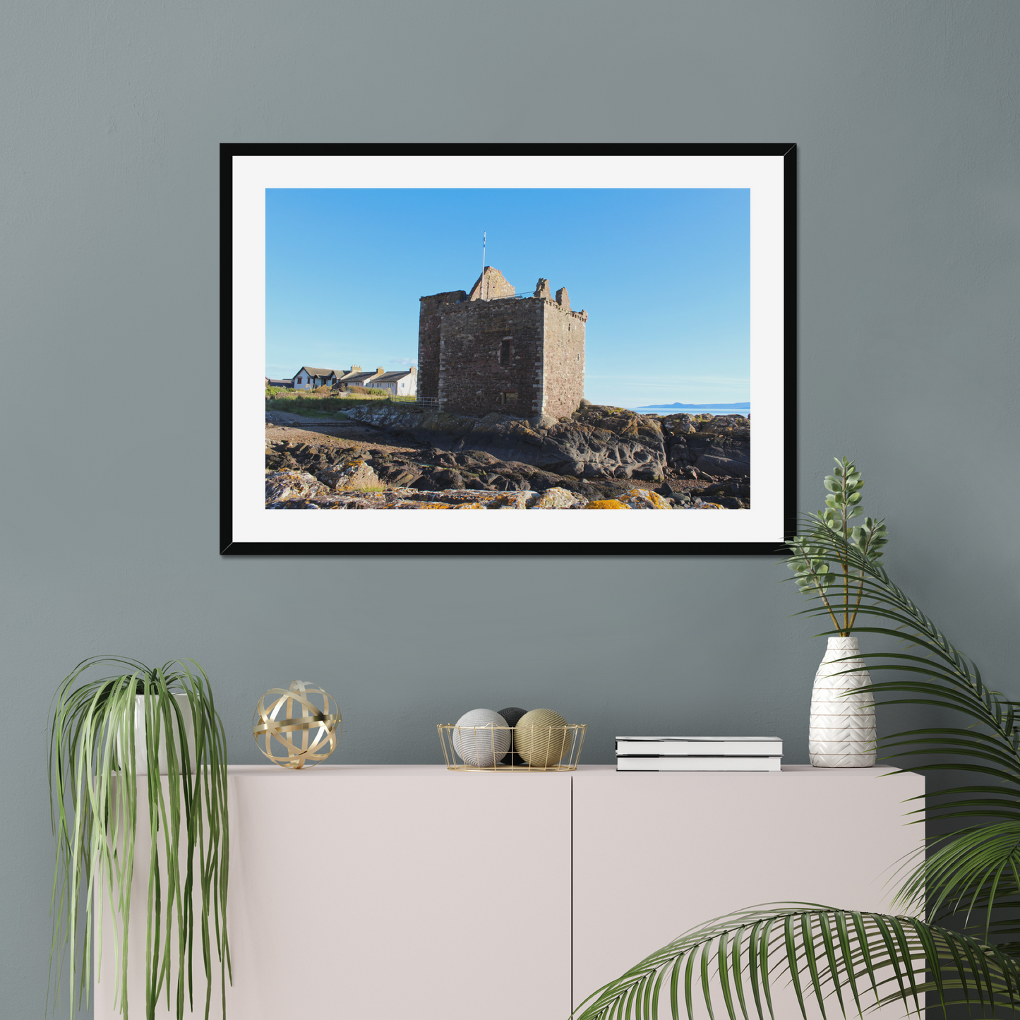 Framed photograph of a castle on a wall above a white cabinet with decorative items.
