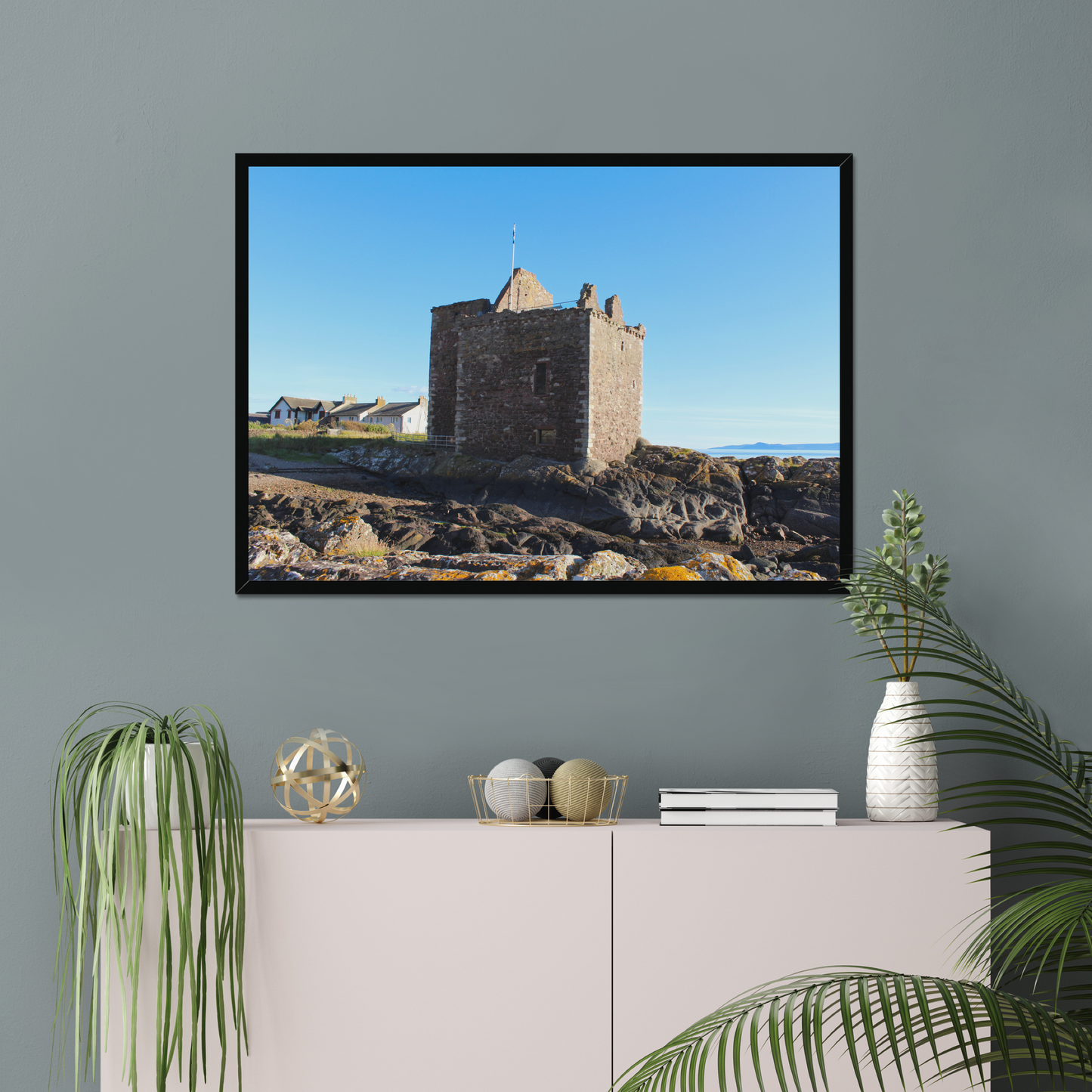 Framed picture of a castle on a wall above a white cabinet with decorative items.