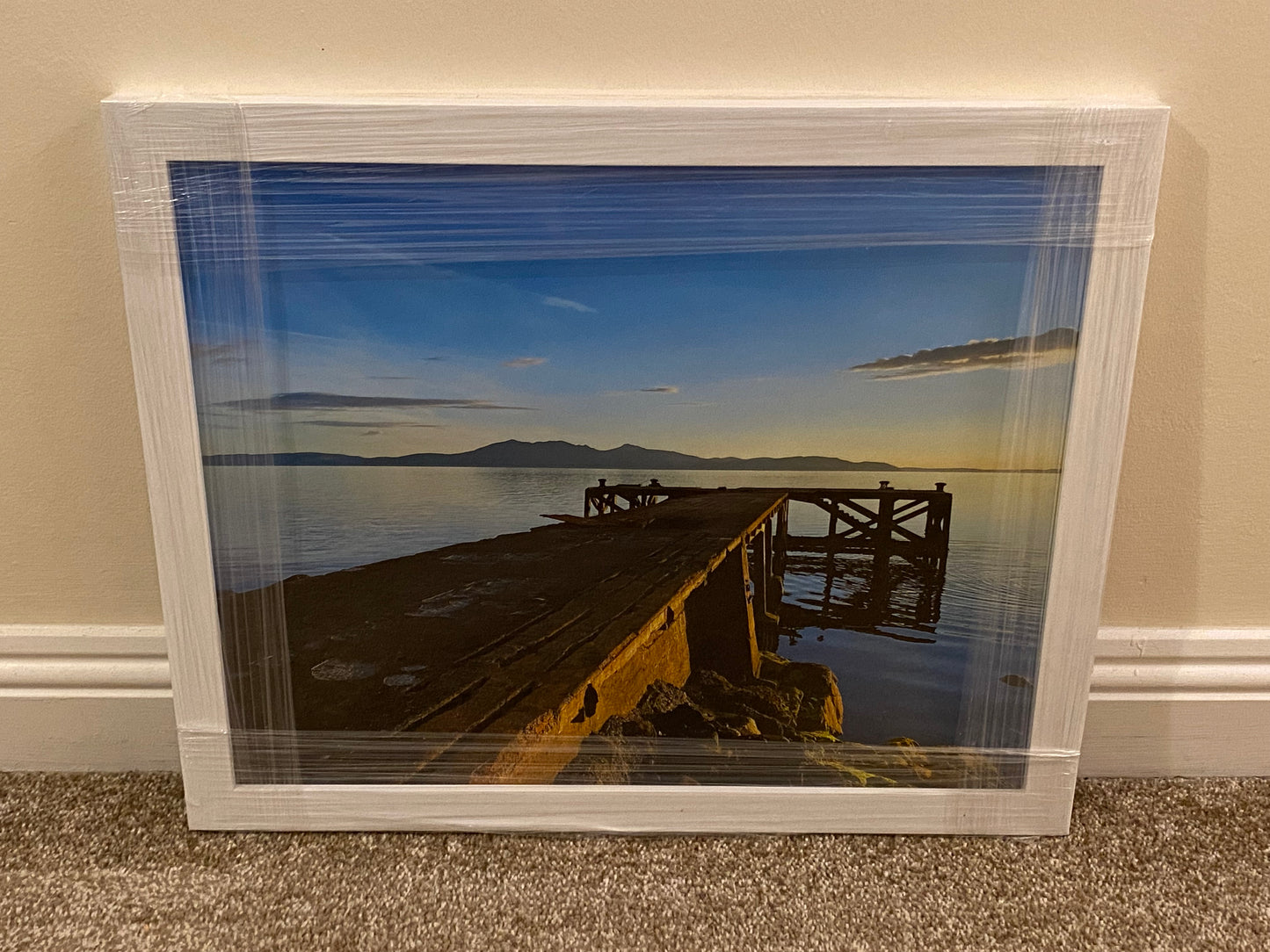 Framed photograph of a dock by a body of water with mountains in the background.