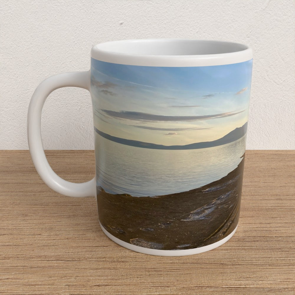 Mug with a scenic design of a beach and sky on a wooden surface.