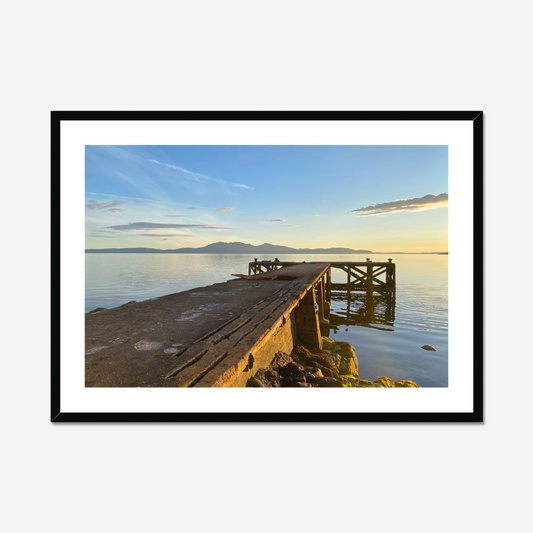 Framed photograph of a dock extending into a calm body of water with mountains in the distance.