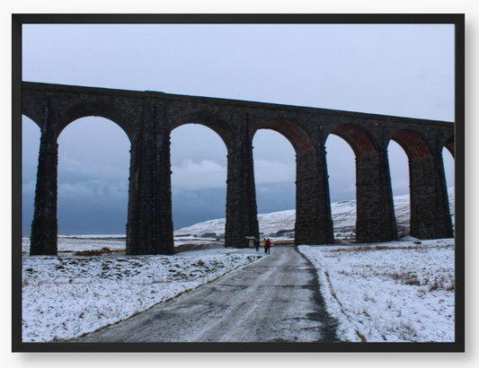 Framed Photo of a Viaduct in a snowy landscape with people walking on a path below.