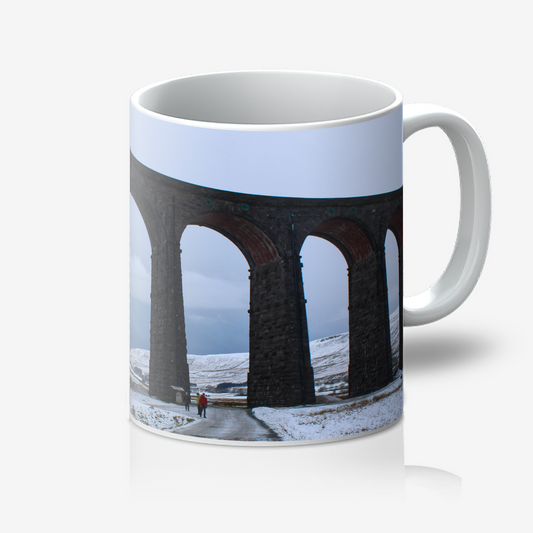 Mug with a design of a snowy landscape featuring a viaduct and people walking on a path.