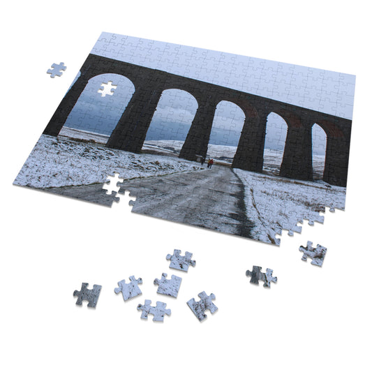 Jigsaw puzzle with a completed section showing a snowy landscape and viaduct, with missing pieces on a white background.