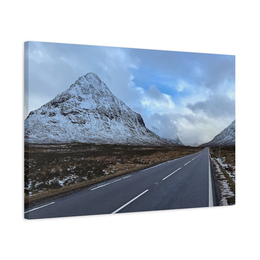 Road leading towards a snow-covered mountain under a cloudy sky