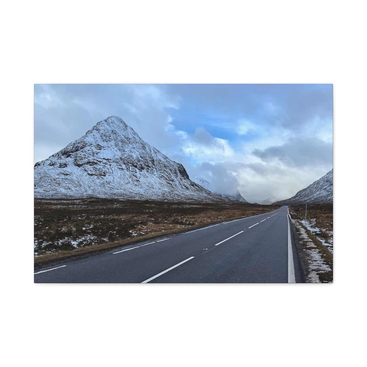 Road leading towards snow-covered mountains under a cloudy sky