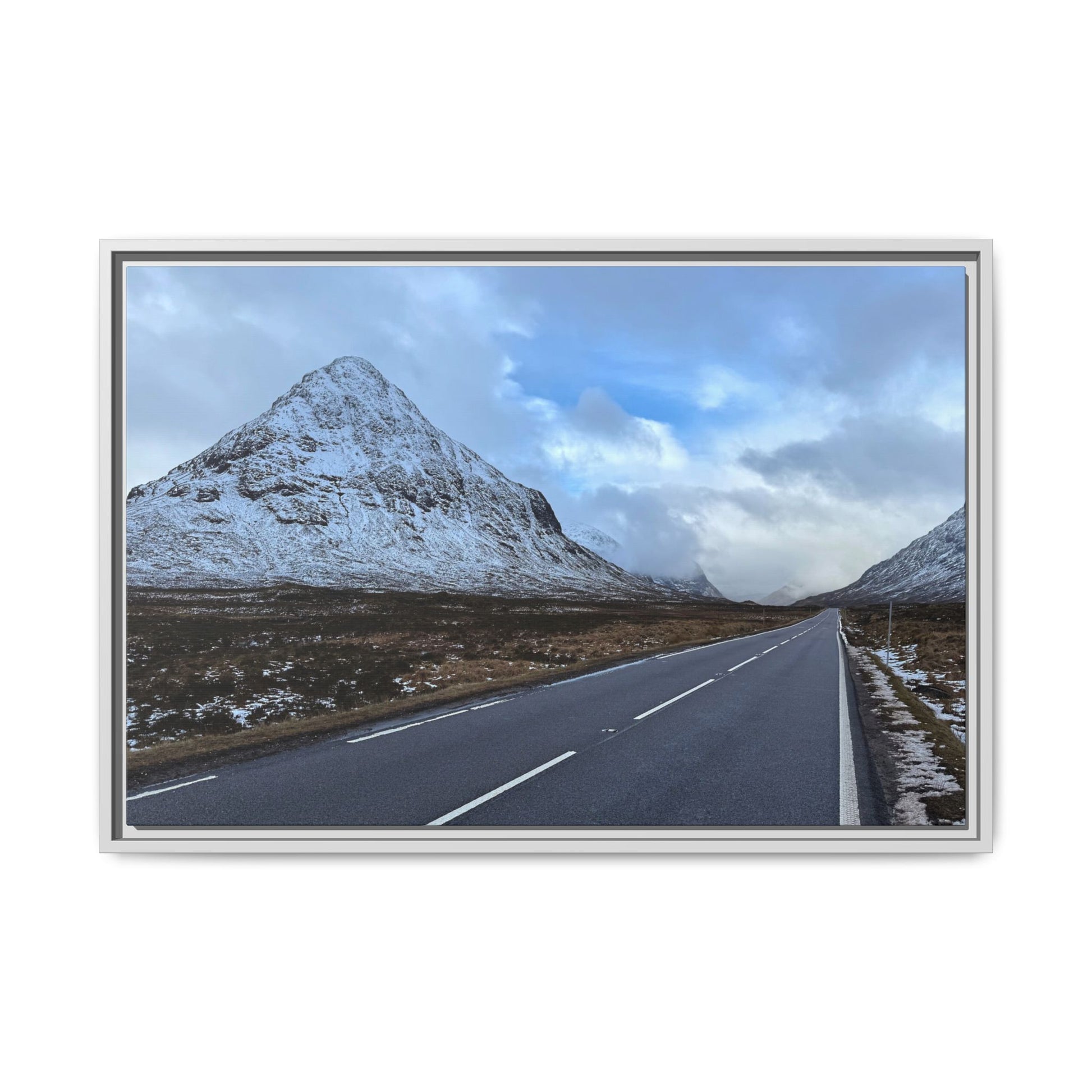 Road leading towards snow-capped mountains under a cloudy sky
