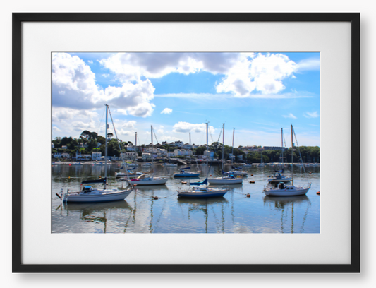 Framed Photo of a Harbour scene with boats docked in calm water under a blue sky with clouds.