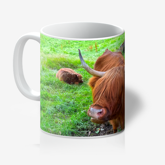 Mug with a design of two Highland cows on a grassy field.