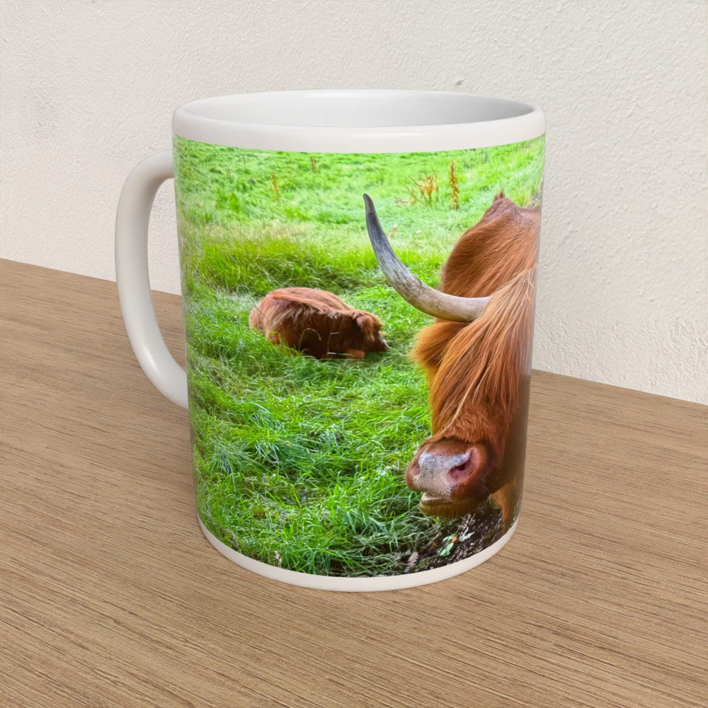 Mug with a design of a cow and calf in a field on a wooden surface.