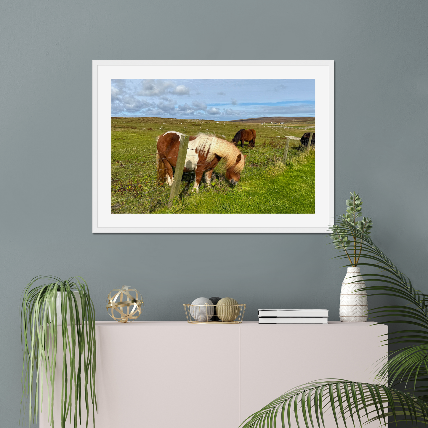 Framed picture of horses grazing on a grassy field hanging on a gray wall.