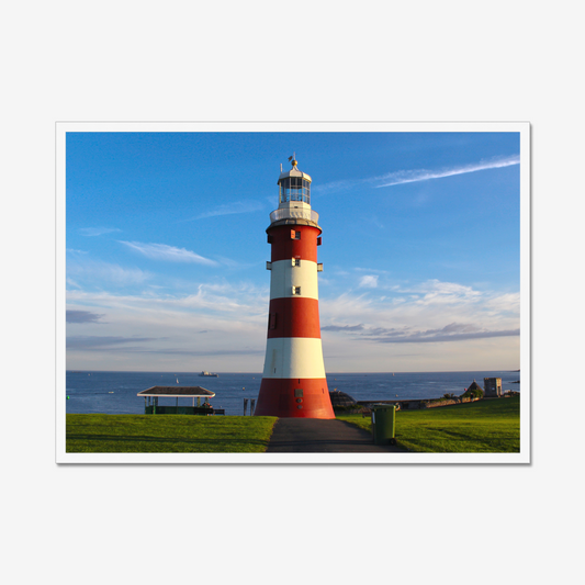 Red and white lighthouse on a grassy area with a blue sky and ocean in the background