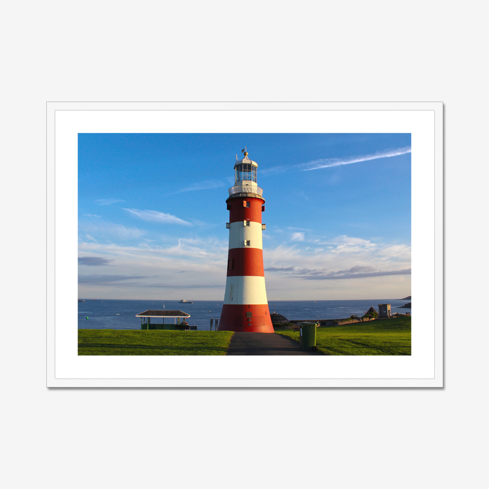 Red and white lighthouse on a grassy area with a blue sky background