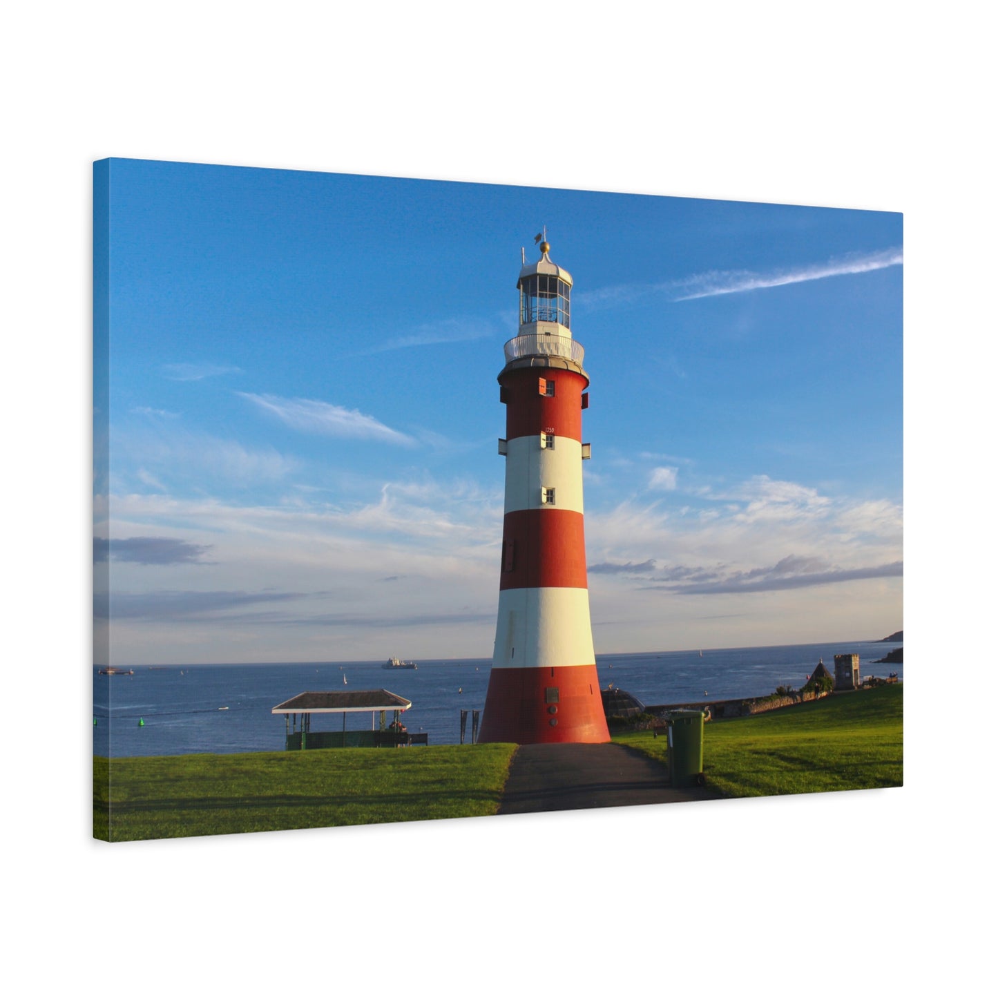 Red and white striped lighthouse on a grassy area with a blue sky.