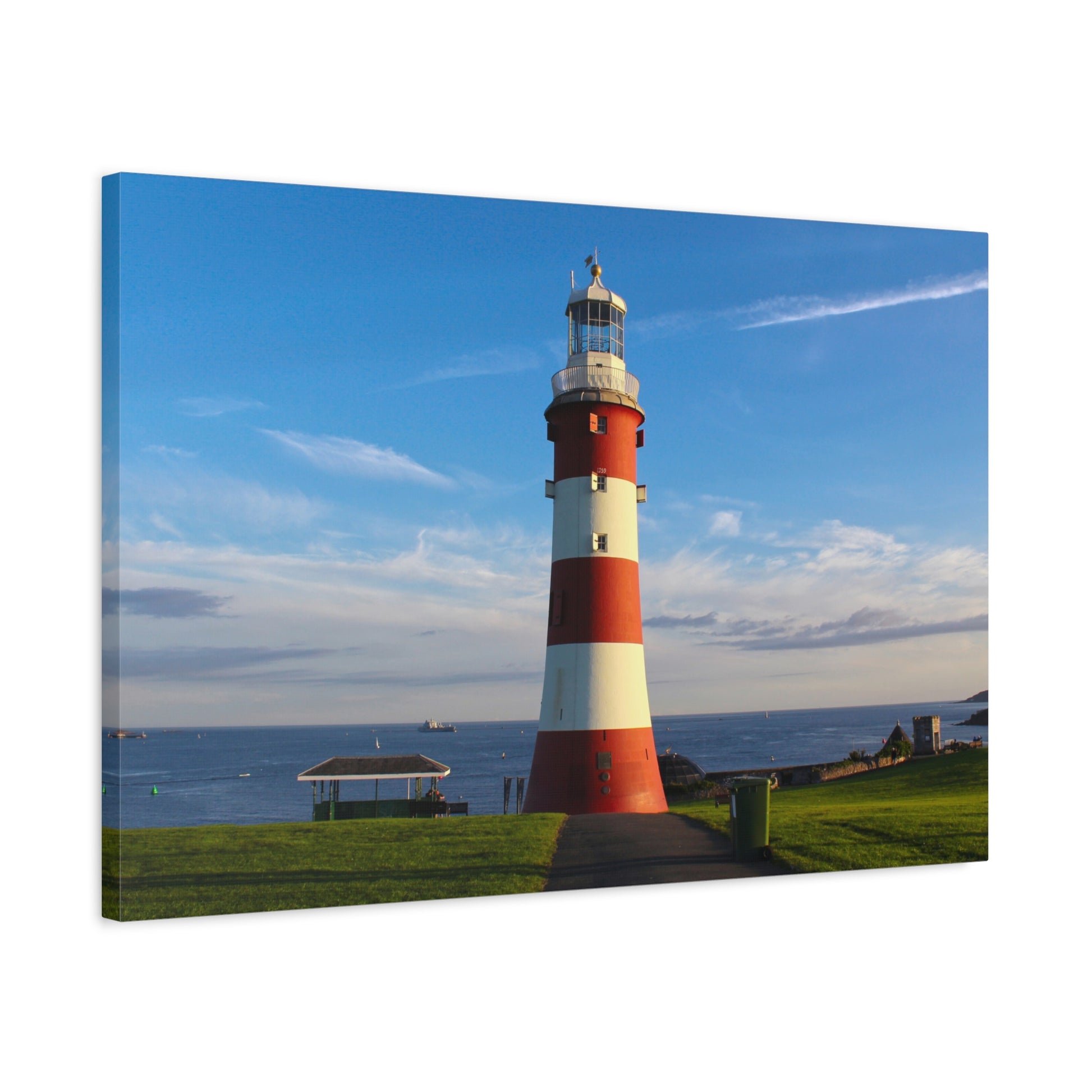 Red and white striped lighthouse on a grassy area with a blue sky.
