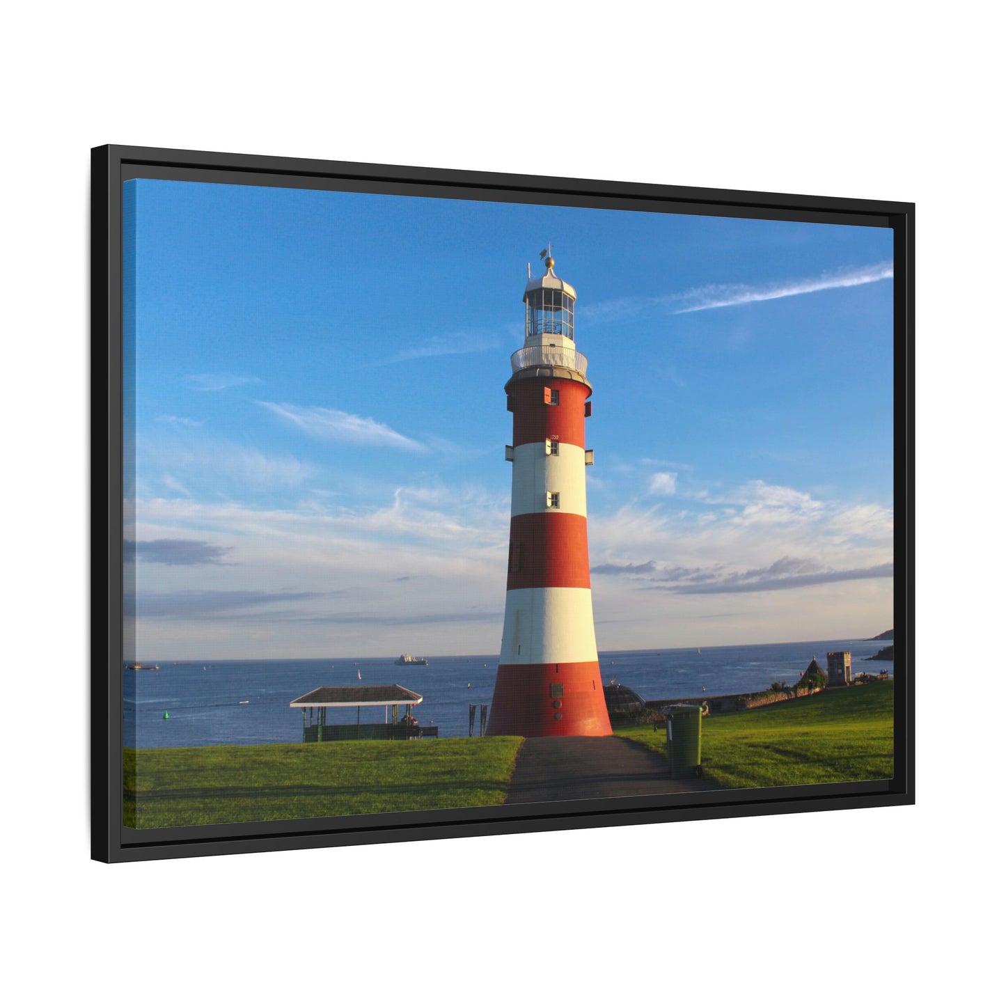 Framed picture of a red and white lighthouse by the sea with a blue sky.