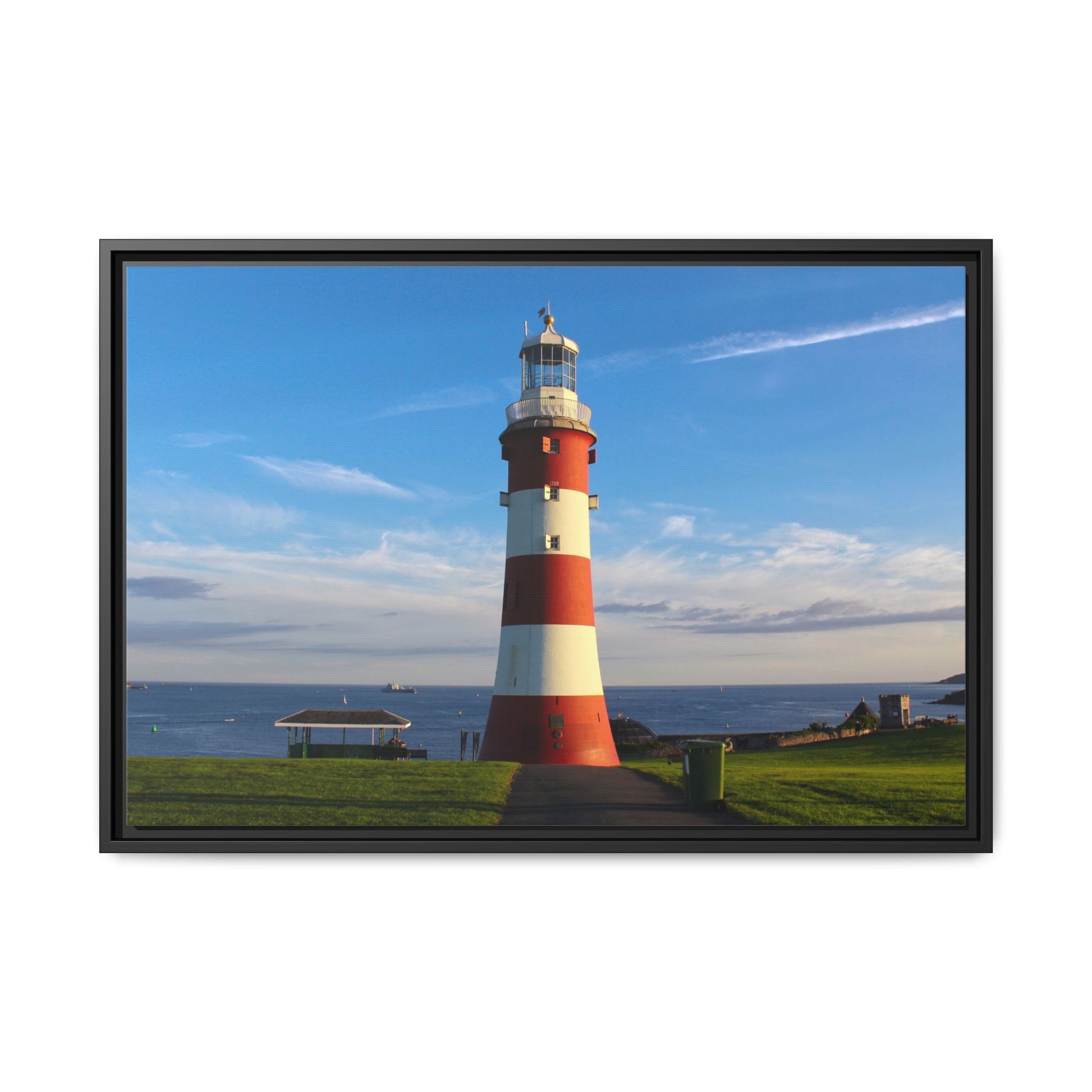Framed picture of a red and white lighthouse by the ocean with a clear blue sky.