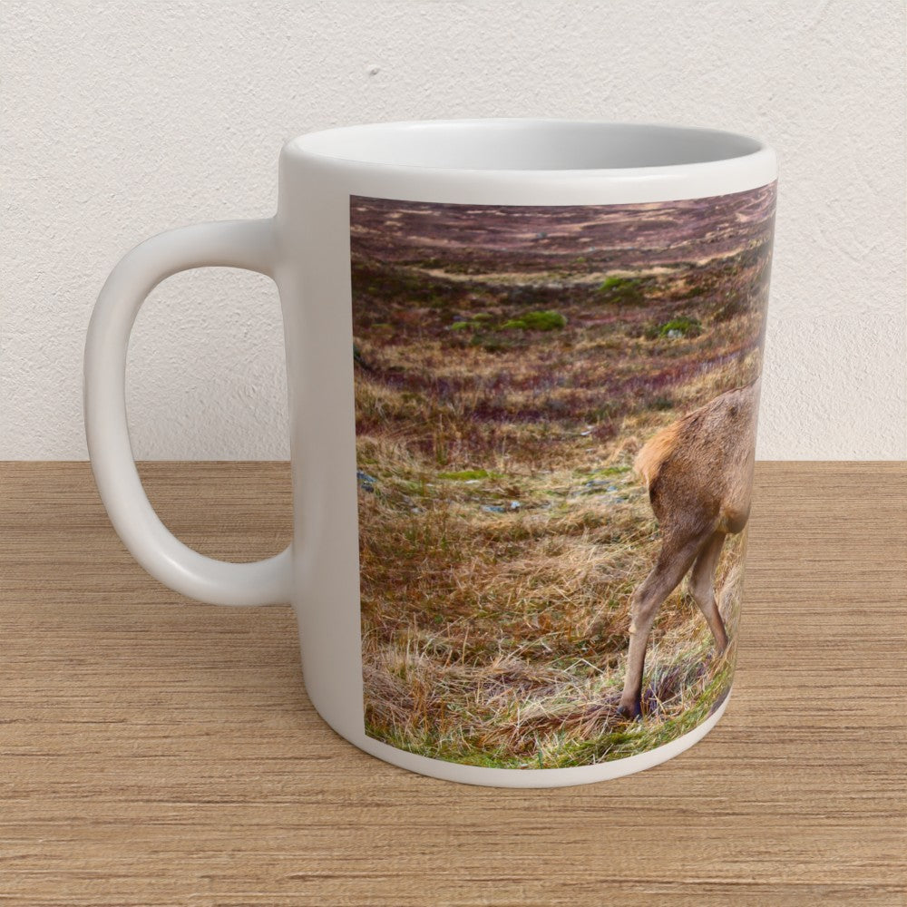White mug with a deer in a field design on a wooden surface