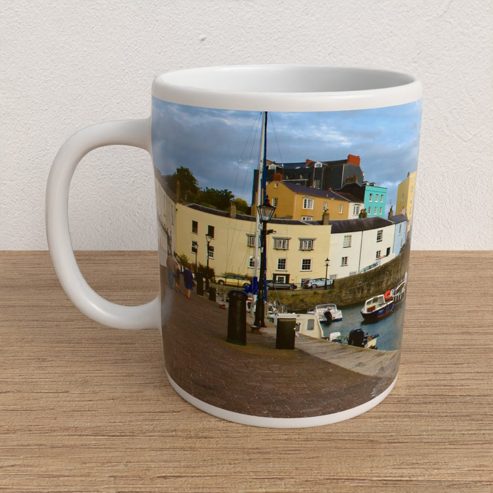 Mug with a scenic print of a harbour and buildings on a wooden surface.