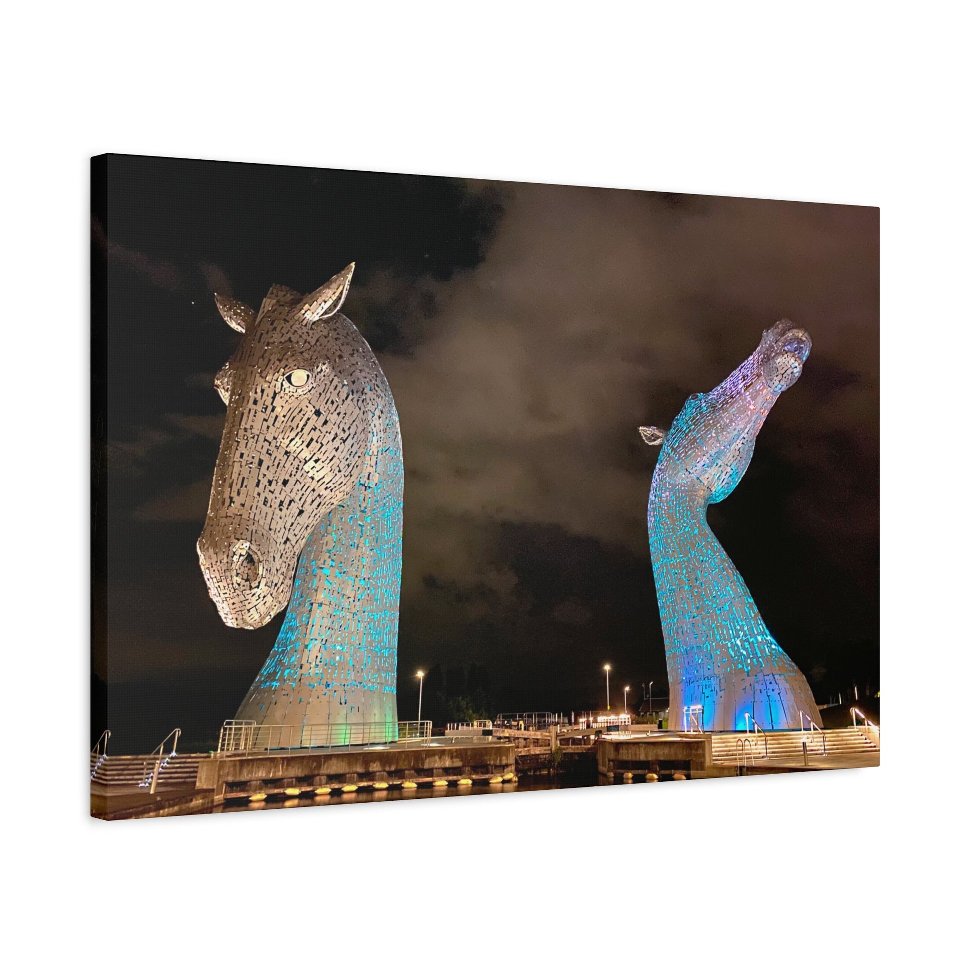Two large horse head sculptures illuminated against a dark sky.