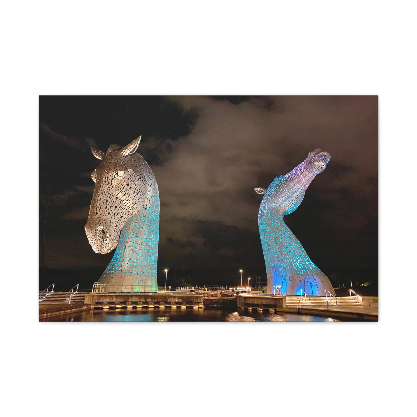 Two large horse head sculptures illuminated at night with a dark sky background.