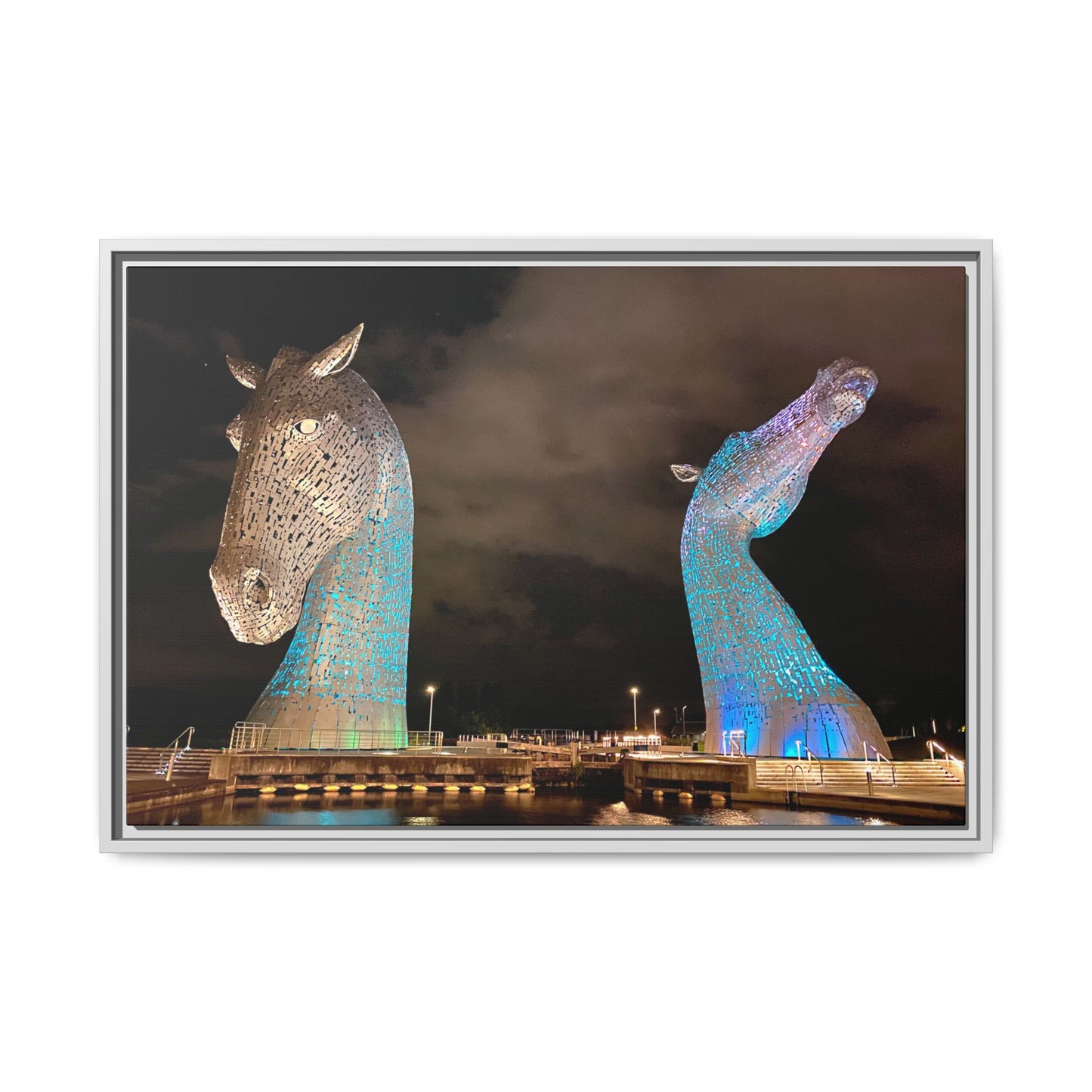 Two large, illuminated horse head sculptures against a dark sky.