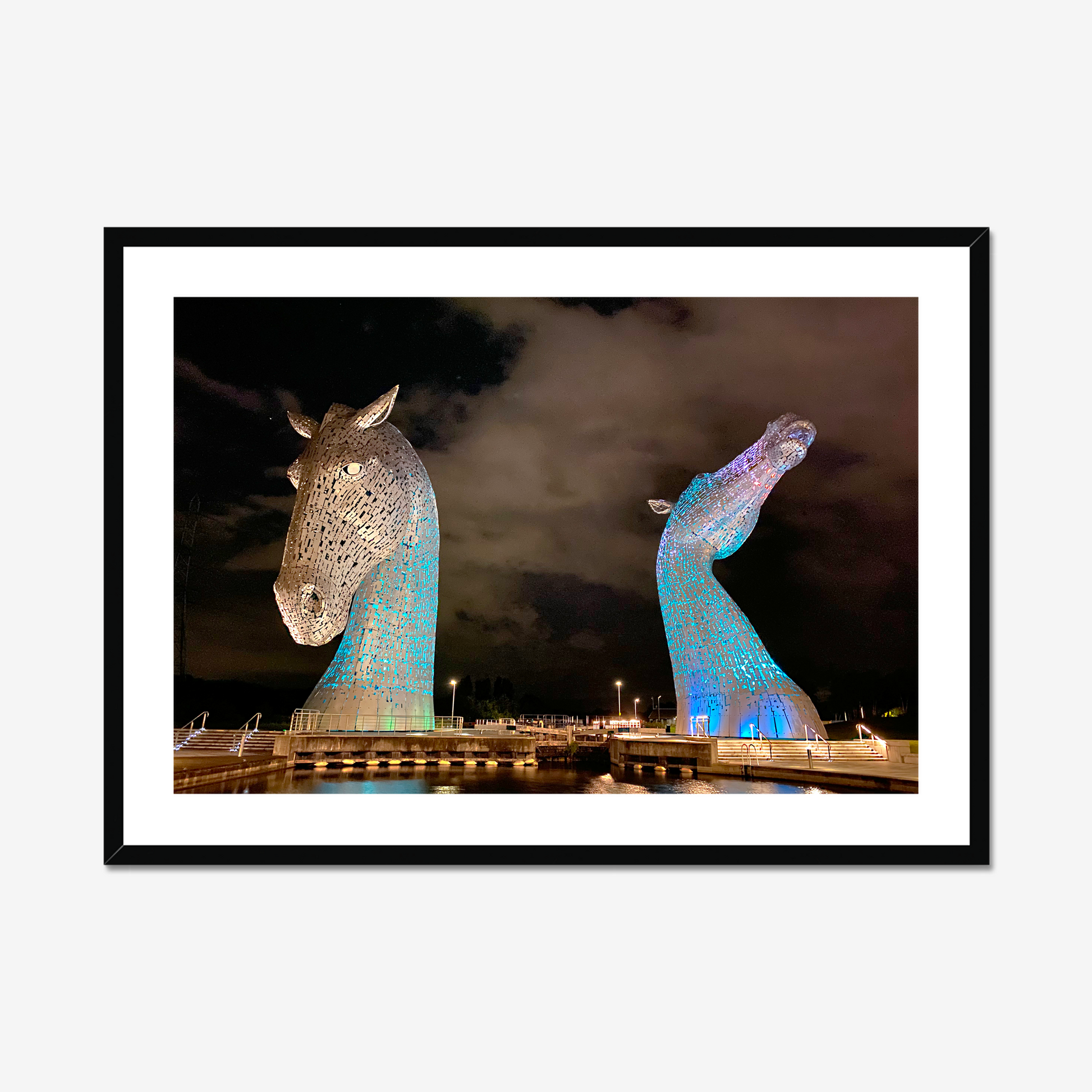 Framed photograph of illuminated horse head sculptures against a dark sky.