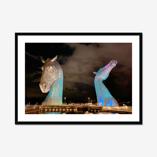 Framed photograph of illuminated horse head sculptures against a dark sky.