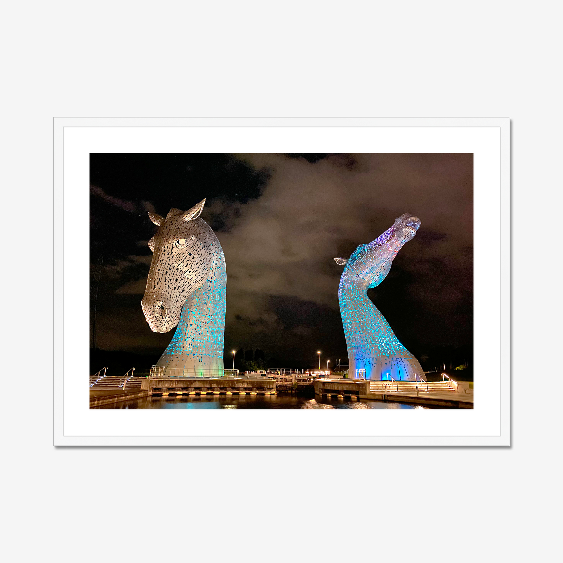 Two large horse head sculptures illuminated at night with a dark sky background.