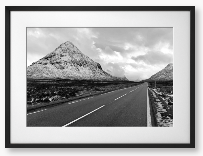 Black and White Framed Photo of a road leading towards snow-capped mountains under a cloudy sky