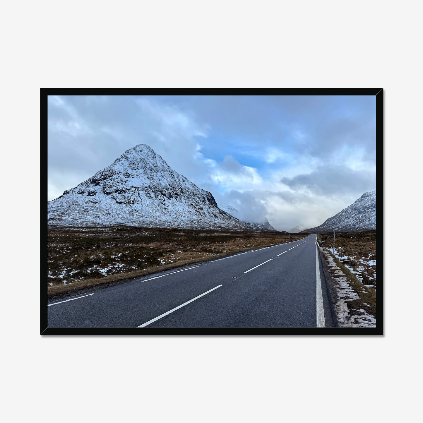 Framed photograph of a road leading towards snow-capped mountains under a cloudy sky