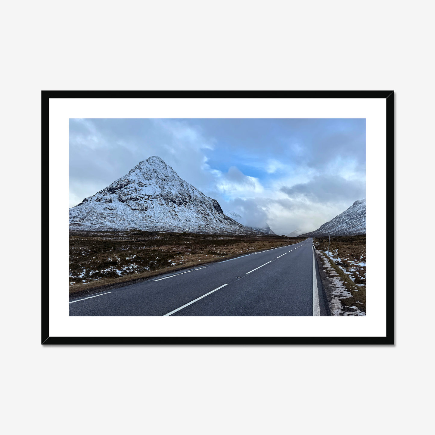 Framed photograph of a road leading towards snow-capped mountains under a cloudy sky