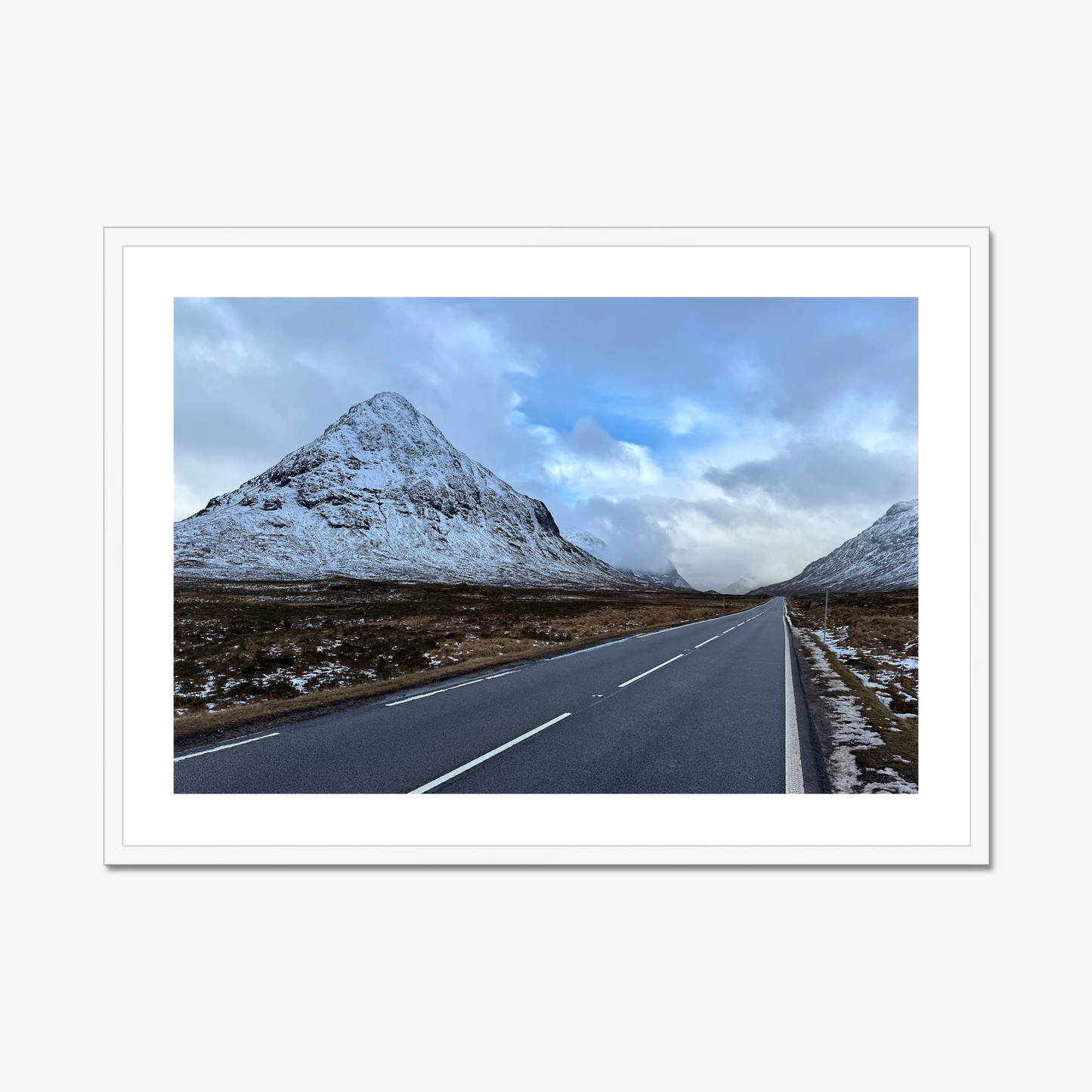 Framed photograph of a road leading towards snow-capped mountains under a cloudy sky