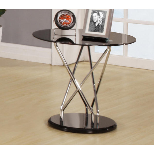 Black glass side table with chrome metal legs in a room setting.