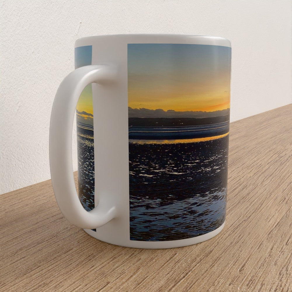 Mug with a scenic design of a sunset over water on a wooden surface.