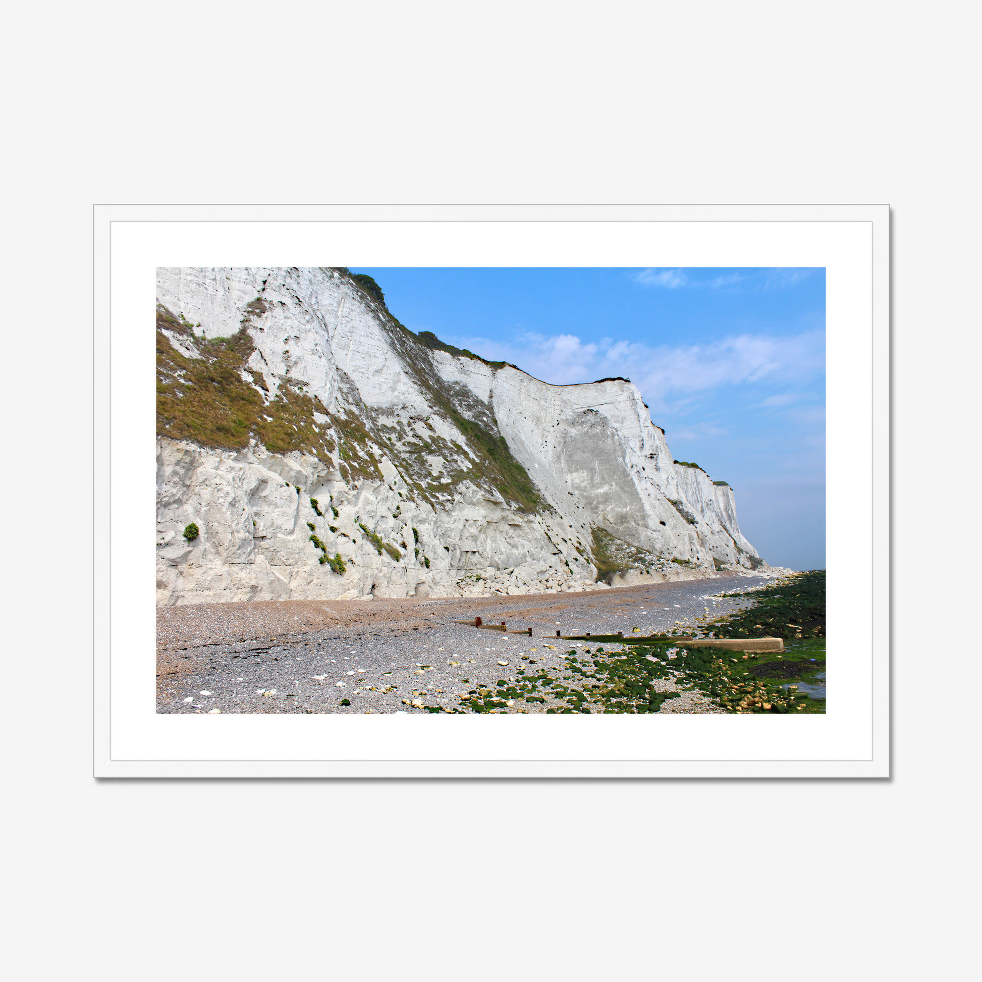 Framed photo of white cliffs with a pebbly beach and blue sky