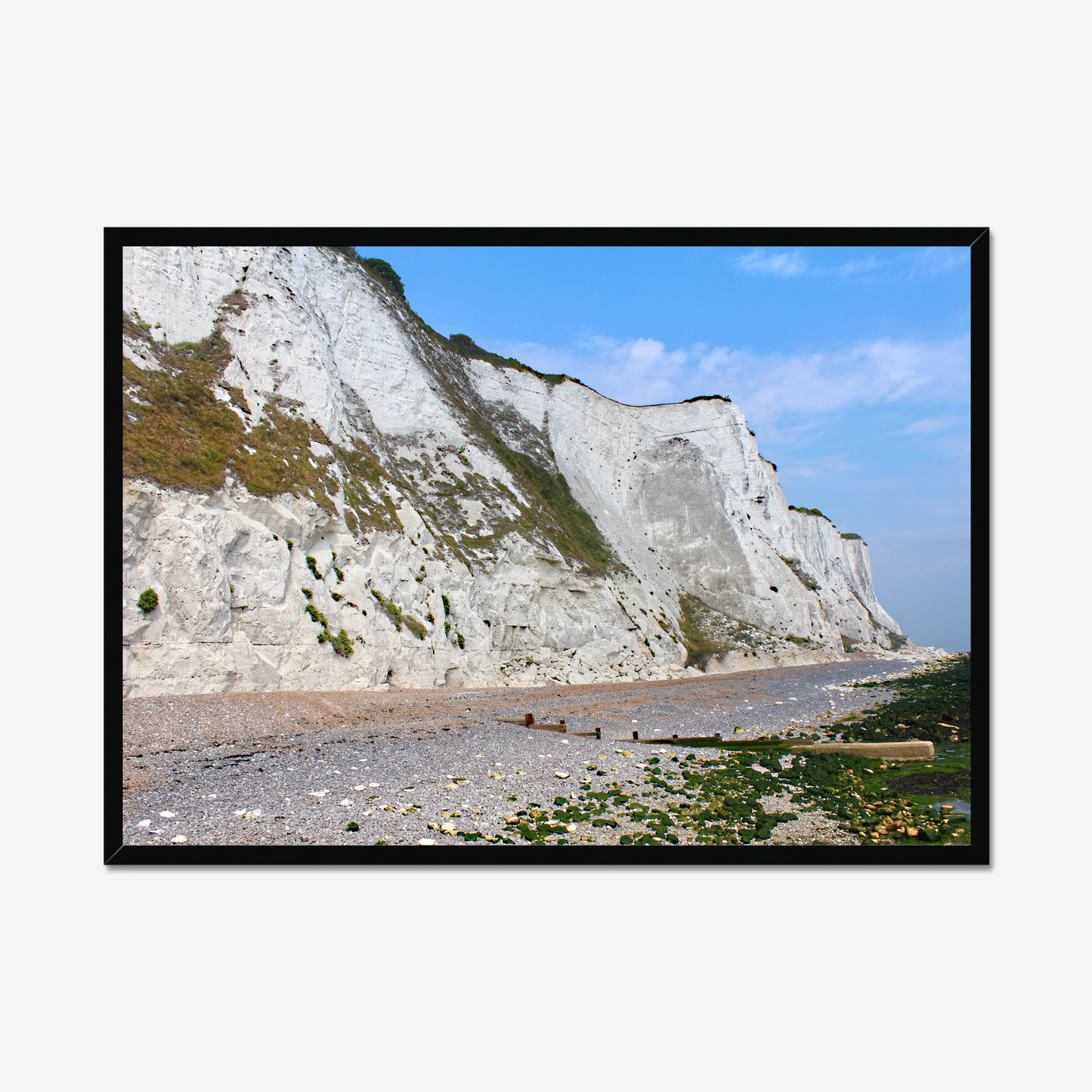 Framed photo of white cliffs with a pebbly beach and blue sky