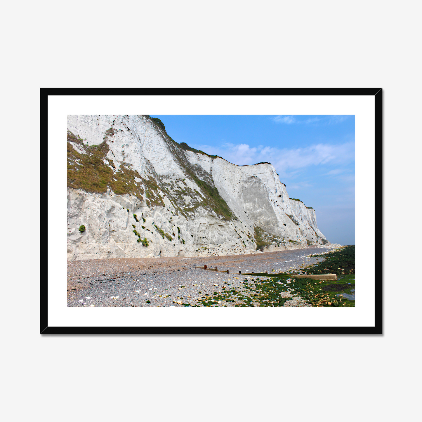 Framed photo of white cliffs with a pebbly beach and blue sky